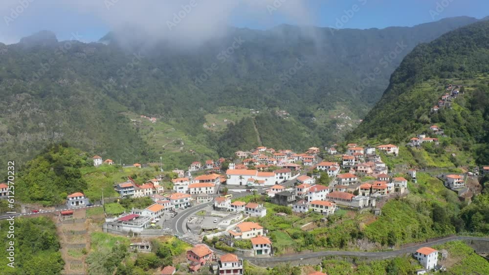 Drone shot of houses on Madeira island landscape with forested and rocky mountains on a sunny day Drone shot of houses on Madeira island landscape with forested and rocky mountains on a sunny day