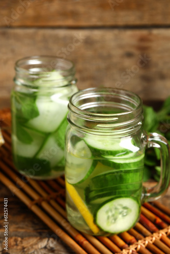 Mason jars of infused water with cucumber slices on wooden background