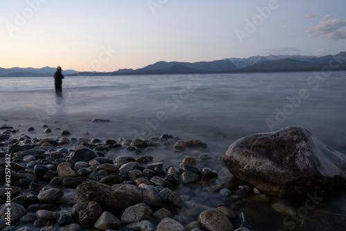 Night shot. View the beautiful water blurred effect and blurred fisherman dark silhouette, fishing at nightfall. The rocky shore and mountains in the horizon with a beautiful dusk light. photo