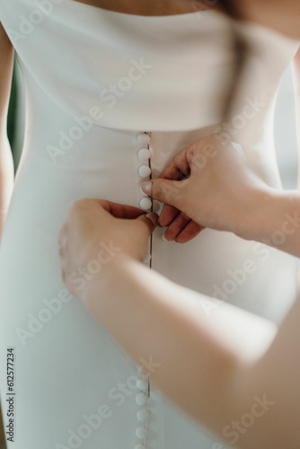 Closeup of hands buttoning bride's dress