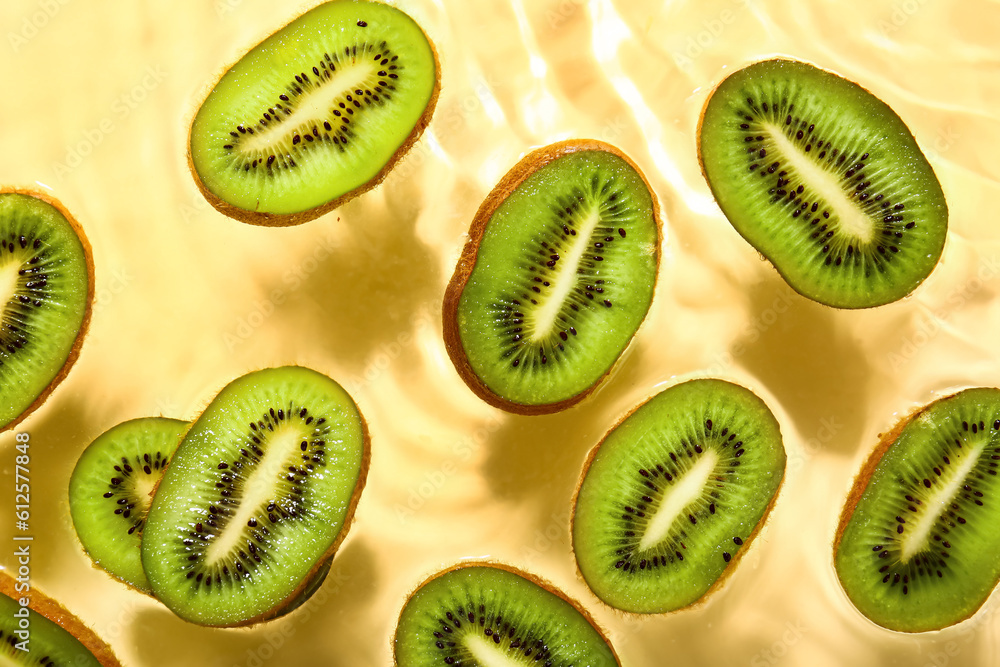 Fototapeta premium Slices of fresh kiwi in water on yellow background