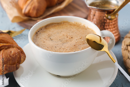 Cup of delicious espresso with jezve and croissant on table, closeup