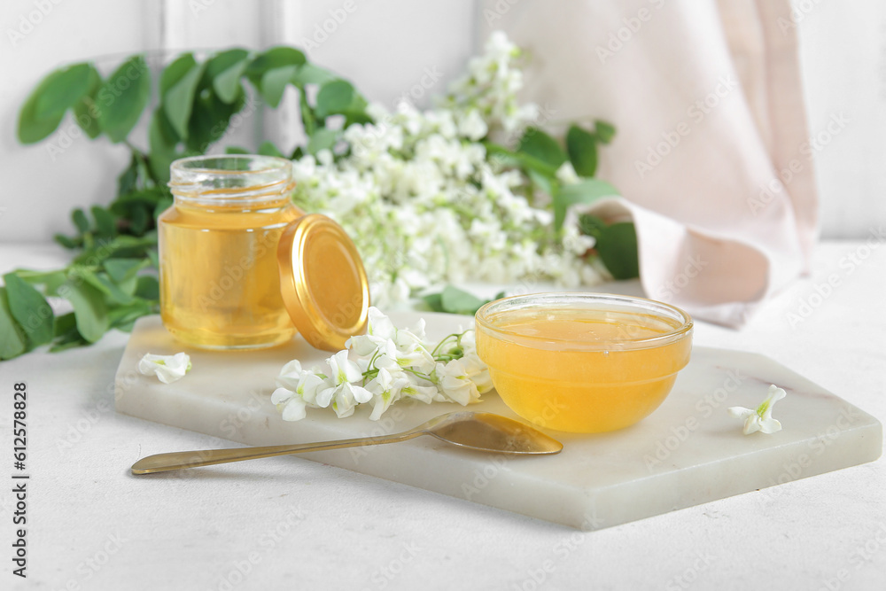 Jar and bowl of honey with flowers of acacia on light background, closeup Jar and bowl of honey with flowers of acacia on light background, closeup