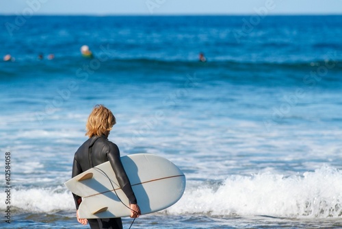 Photography Person standing at the shore of the sea with splashing waves with a surfing boar