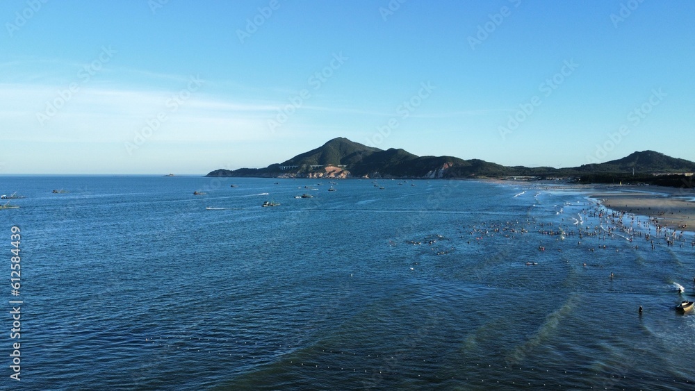 Drone view of the seascape surrounded by hills and a sandy shore with people in the daytime