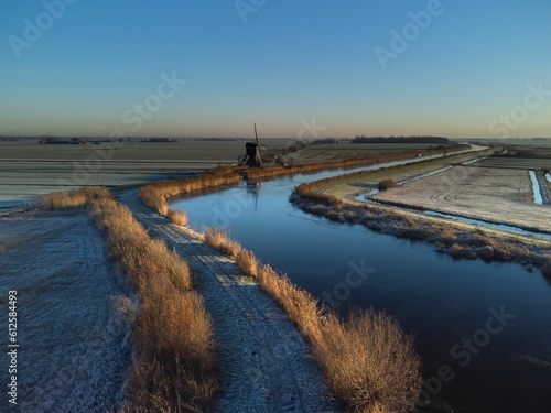 Winter landscape of a river along the frosty fields and an old windmill in the background