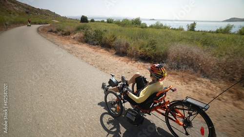 Rear view of elderly senior woman riding recumbent e-bike electric tricycle bicycle beside a lake on a sunny day beside a lake with mountains in the distance. photo