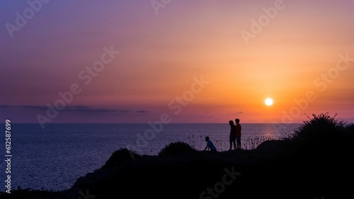 Silhouettes of children on the coast of a sea at a bright orange sunset