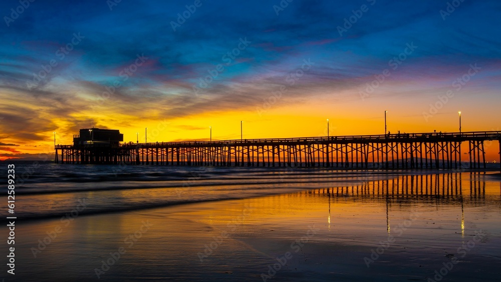 Fototapeta premium Distant shot of a pier over a sea before the golden sunset in the evening