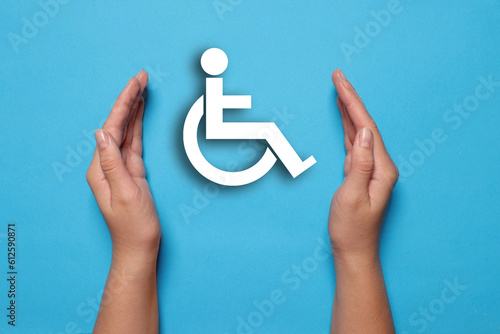 Disability inclusion. Woman protecting wheelchair symbol on light blue background, closeup