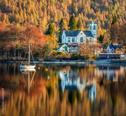 Scenic shot of a ship on the lake with a lush autumn forest and big houses on the background