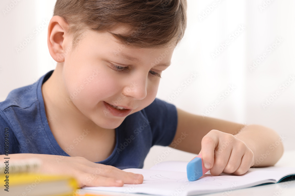Little boy erasing mistake in his notebook at white desk indoors Little boy erasing mistake in his notebook at white desk indoors