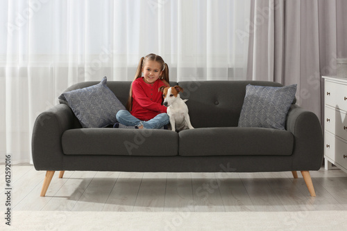 Cute girl with her dog on sofa at home. Adorable pet