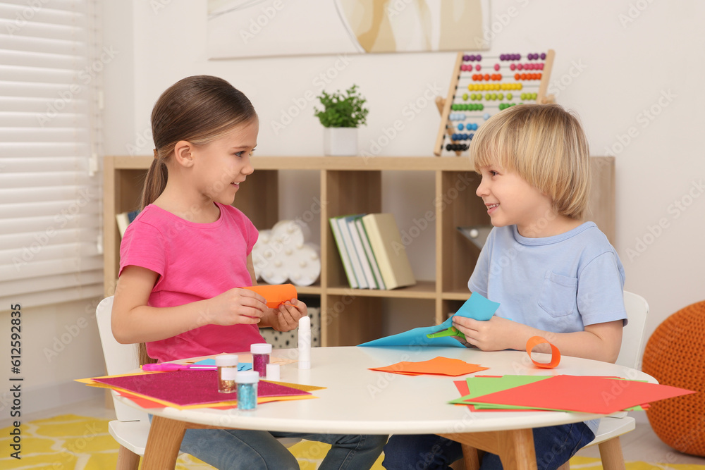 Cute children making paper toys at desk in room. Home workplace Cute children making paper toys at desk in room. Home workplace