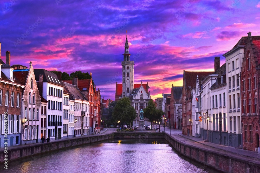 Scenic purple sunset over the houses and the Poortersloge on the bank of a river in Bruges, Belgium