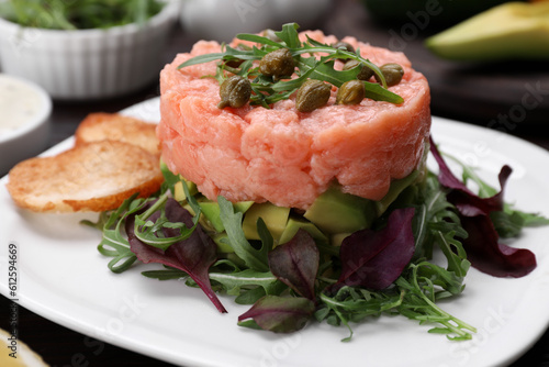 Tasty salmon tartare with avocado, greens and croutons on table, closeup