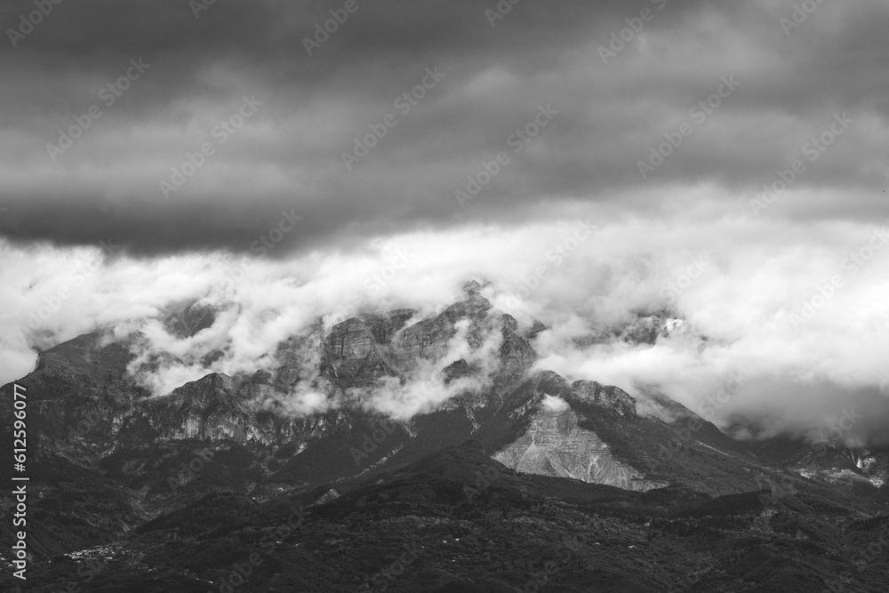 Grayscale of a mountain peak covered in fog with a cloudy dramatic sky in the background