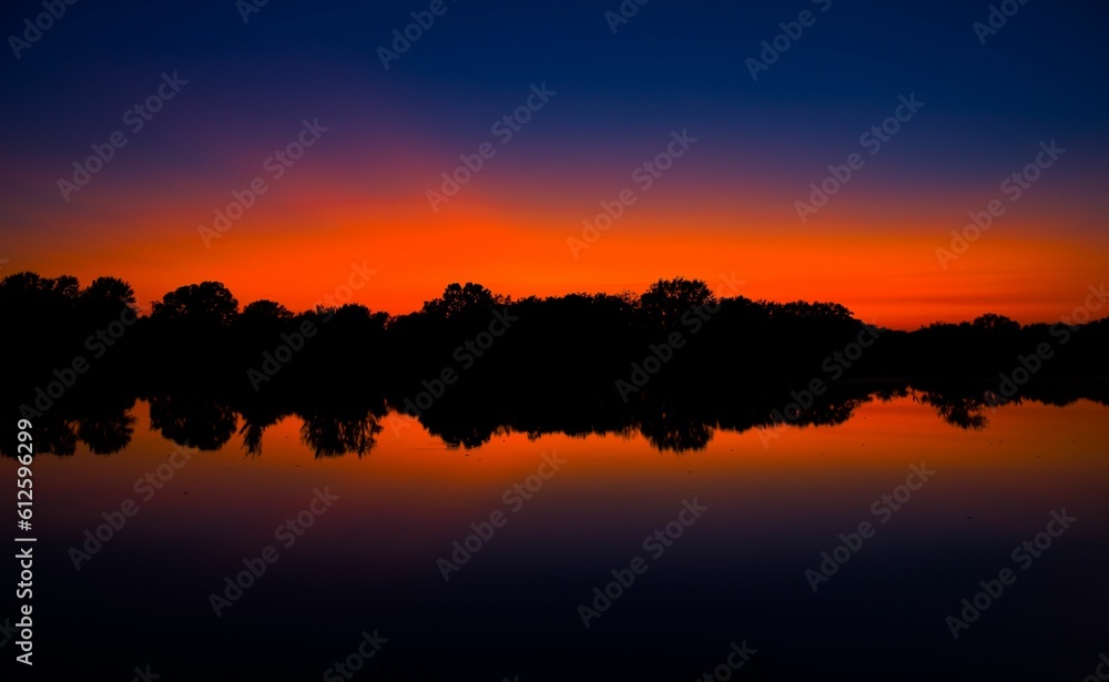 Glow of a summer sunset silhouetting the treeline reflecting into the lake