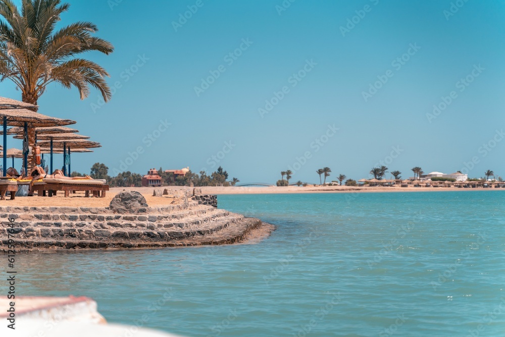 Peoply lying at the Sultan Bay El Gouna Beach with straw umbrellas and palms