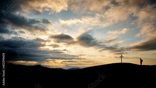 Beautiful shot of a silhouette of a hiker reaching a cross on a field at sunset in Tyrol