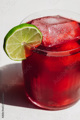 agua de Jamaica, hibiscus tea drink with ice in rocks glass, lime wheel garnish, white background with sunlight photo