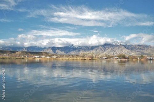 Beautiful natural landscape of high mountains next to farmlands near blue lake reflecting cloudy sky