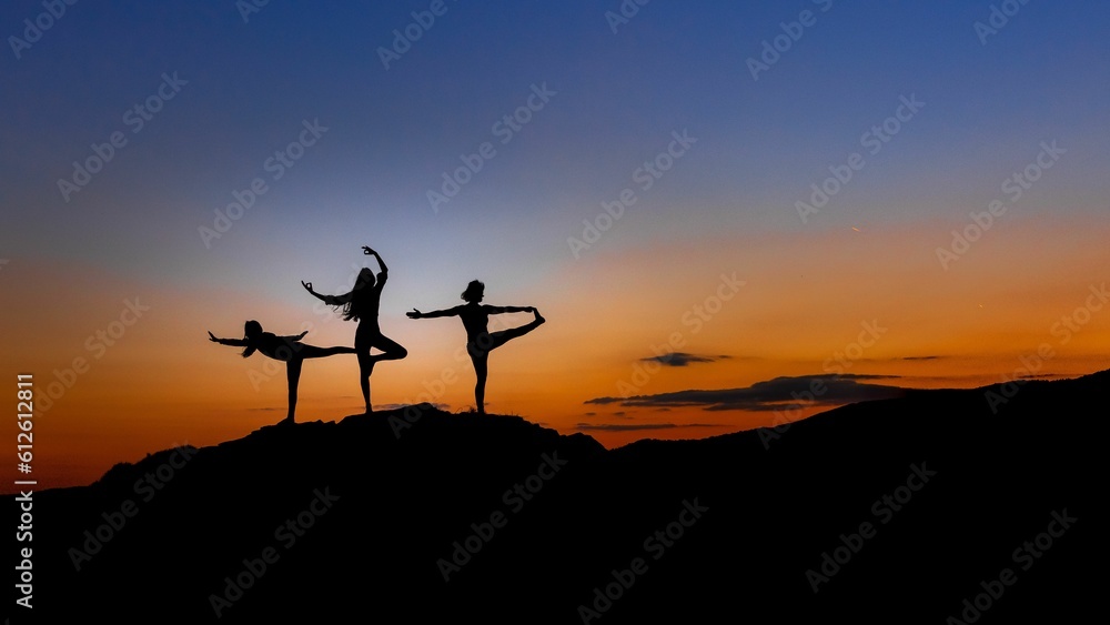 Beautiful shot of a silhouette of people doing yoga on a mountain at sunset