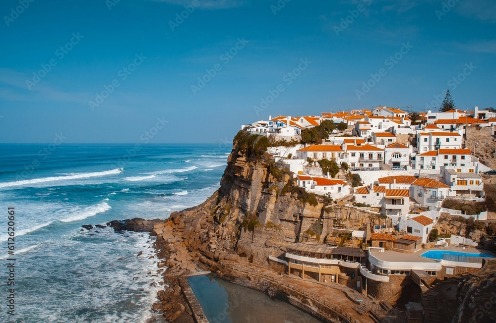 Aerial shot of white buildings with red roofs on a cliff by a sea in Azenhas do Mar, Portugal