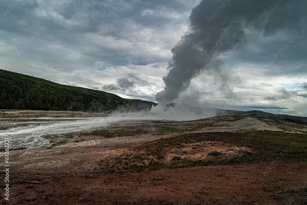 Scenic view of white smoke from a geyser with green mountain in the background on a cloudy day Scenic view of white smoke from a geyser with green mountain in the background on a cloudy day