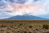 Large desert field with mountains on the horizon under rainy clouds in the background