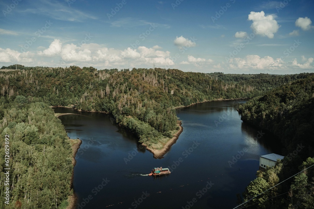 Arial view of riverboat near wooded area, sunlit landscape