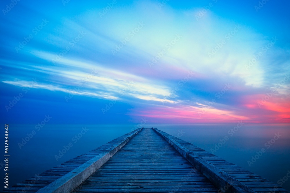 Long wooden pier extends out into a tranquil body of water during the pink and blue sunset