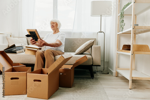 elderly woman sits on a sofa at home with boxes. collecting things with memories albums with photos and photo frames moving to a new place cleaning things and a happy smile. Lifestyle retirement. © SHOTPRIME STUDIO