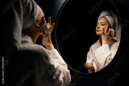 Woman smearing cream on face at night
