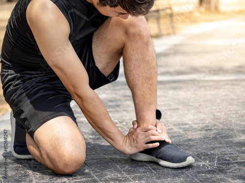 Asian athlete man touching foot in pain due to sprained ankle while running in the park. Broken twisted ankle sprain or foot cramp. Sport injury concept photo