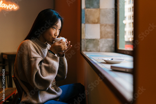 Calm Asian woman drinking hot coffee in cafe