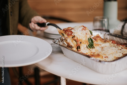 Woman serves a portion cooked lasagna from a tray.