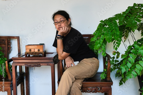 A middle-aged woman sitting in a wooden chair; thinking, serious expression photo