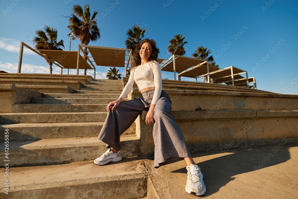 Cheerful cool young woman sitting on stairs in city park Cheerful cool young woman sitting on stairs in city park