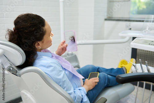 Smiling pregnant woman, female patient sitting in dentist's chair, looking in the mirror after professional dental treatment in dentistry clinic. Dental practice. Caries prevention and teeth treatment
