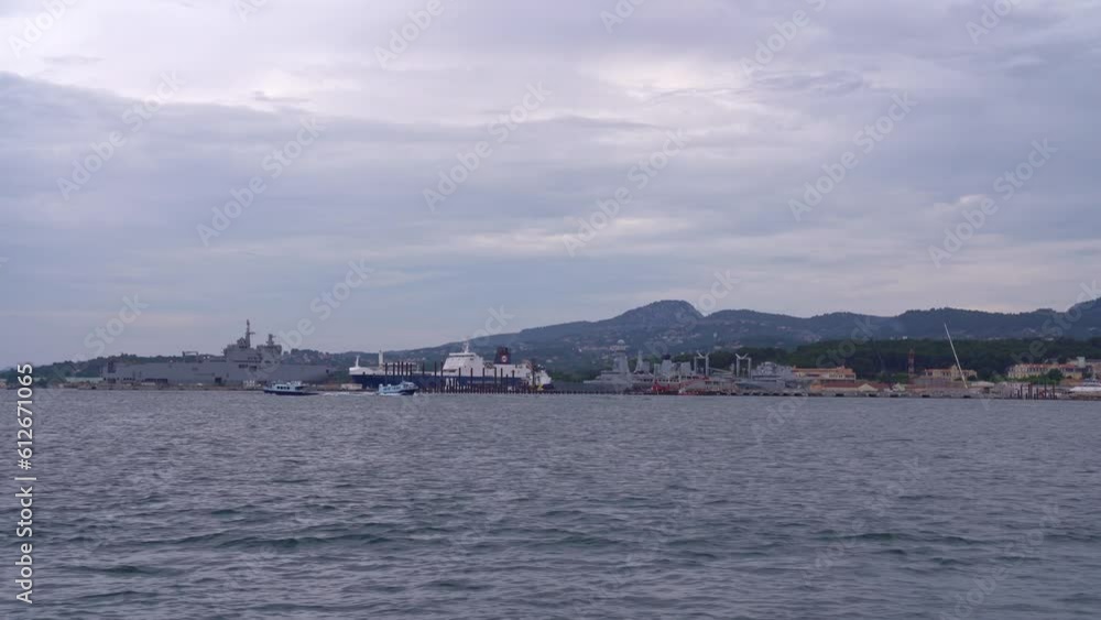 Harbor with moored war ships of French Navy with mountain panorama in the background on a cloudy late spring day at City of Toulon. Movie shot June 9th, 2023, Toulon, France. Harbor with moored war ships of French Navy with mountain panorama in the background on a cloudy late spring day at City of Toulon. Movie shot June 9th, 2023, Toulon, France.