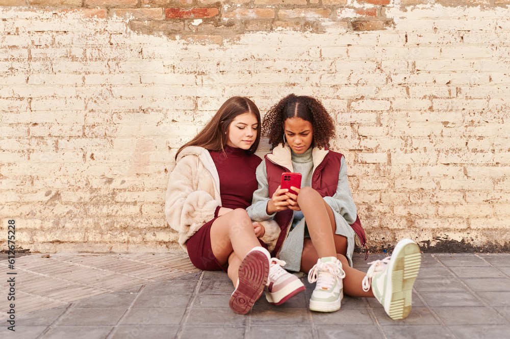 Teens using a phone on a city sidewalk Teens using a phone on a city sidewalk