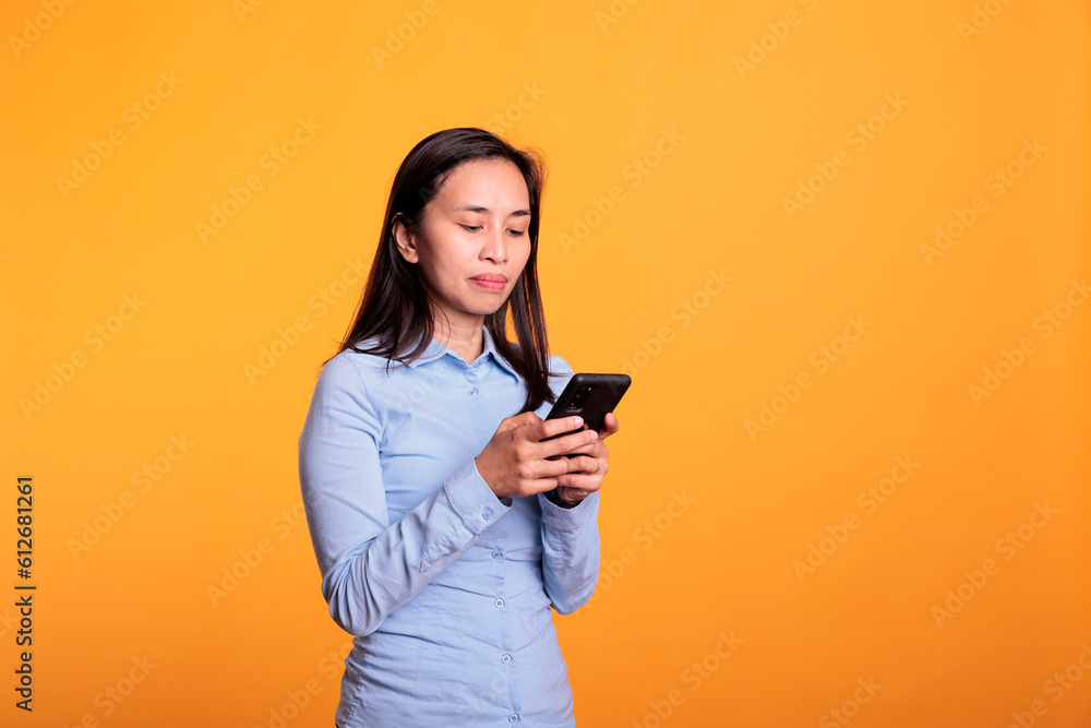 Asian woman chatting with remote friend using smartphone, typing message during work break in studio over yellow background. Cheerful young adult browsing on social media, searching information Asian woman chatting with remote friend using smartphone, typing message during work break in studio over yellow background. Cheerful young adult browsing on social media, searching information