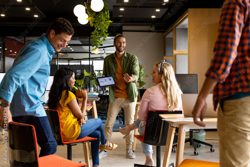 Caucasian casual businessman presenting to diverse colleagues using tablet in office