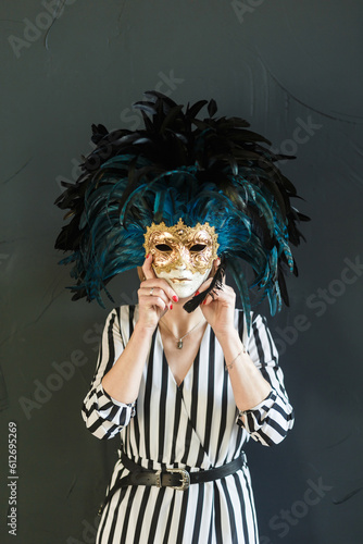 woman holds a carnival mask covering her face