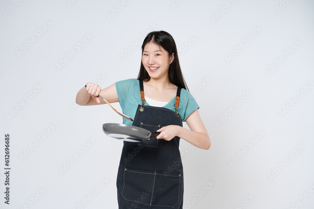 Naklejka premium Young woman wearing kitchen apron cooking and holding pan and spatula isolated on white background.