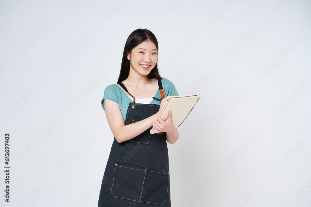 Young woman wearing kitchen apron holding notepad recipe cooking book and pen isolated on white background. Young woman wearing kitchen apron holding notepad recipe cooking book and pen isolated on white background.