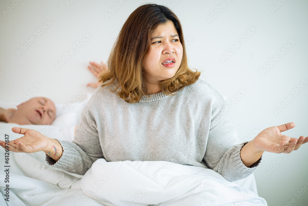 Woman suffers from her male partner snoring while lying in bed together. Snoring is one of the factors of sleep deprivation. Woman suffers from her male partner snoring while lying in bed together. Snoring is one of the factors of sleep deprivation.