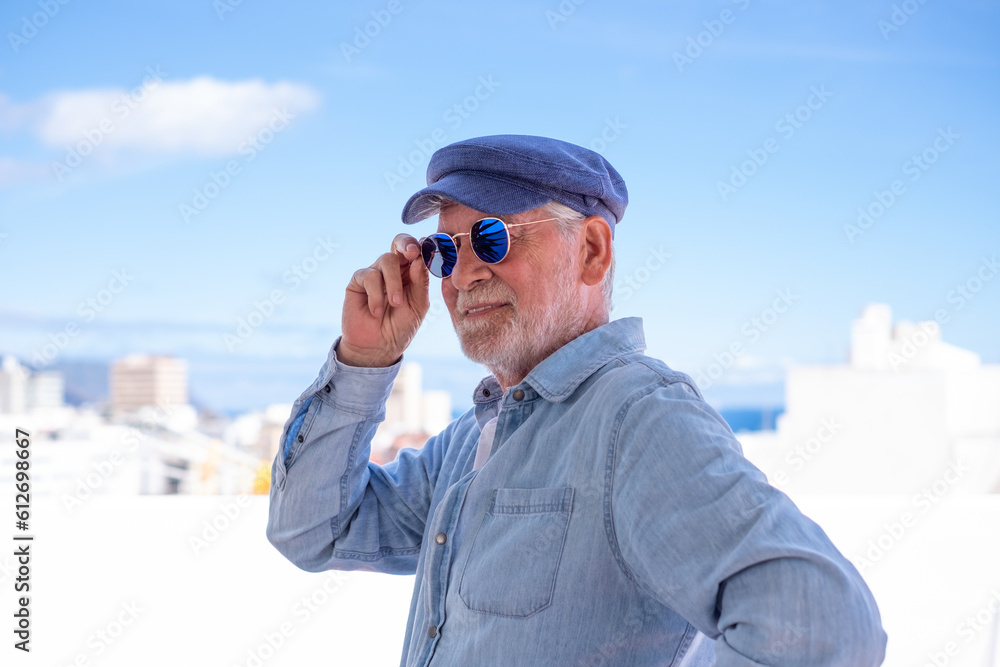 Portrait of senior man smiling and looking away. Face of a happy old man wearing blue sunglasses and cap outdoor. Retired relaxed man with white hair and beard in denim shirt Portrait of senior man smiling and looking away. Face of a happy old man wearing blue sunglasses and cap outdoor. Retired relaxed man with white hair and beard in denim shirt