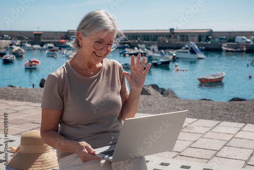 Video call concept. Elderly woman sitting at the port using laptop in video chat with family or friends. Old people and new technologies, senior lady in virtual connection